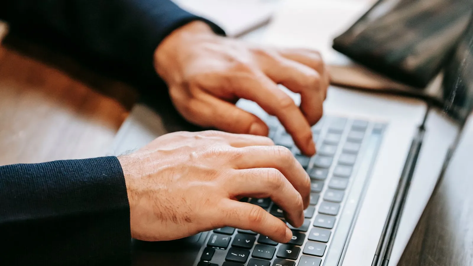 Hands typing on a laptop keyboard on a wooden desk