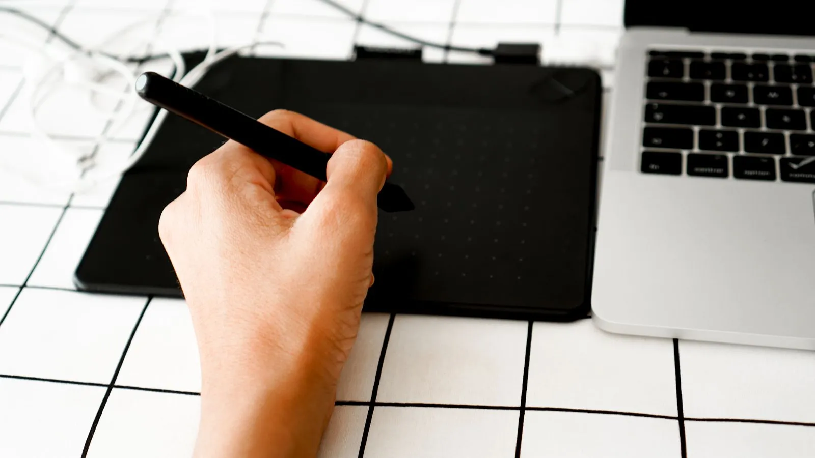 Hand holding a pen over a graphics tablet next to a laptop
